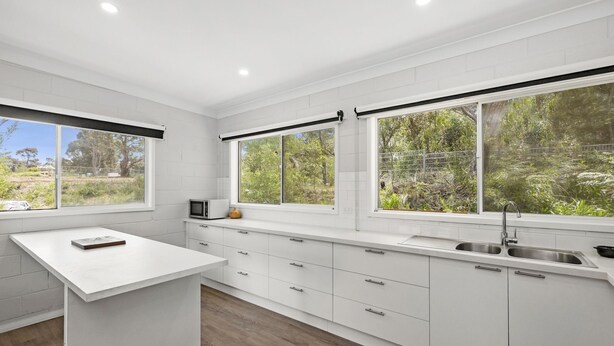 Una cocina moderna con armarios blancos, una isla central y grandes ventanales con vistas al verdor.
