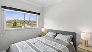Un dormitorio con un ventanal grande, una cama con ropa de cama a rayas, dos lámparas de noche y una mesita de noche.