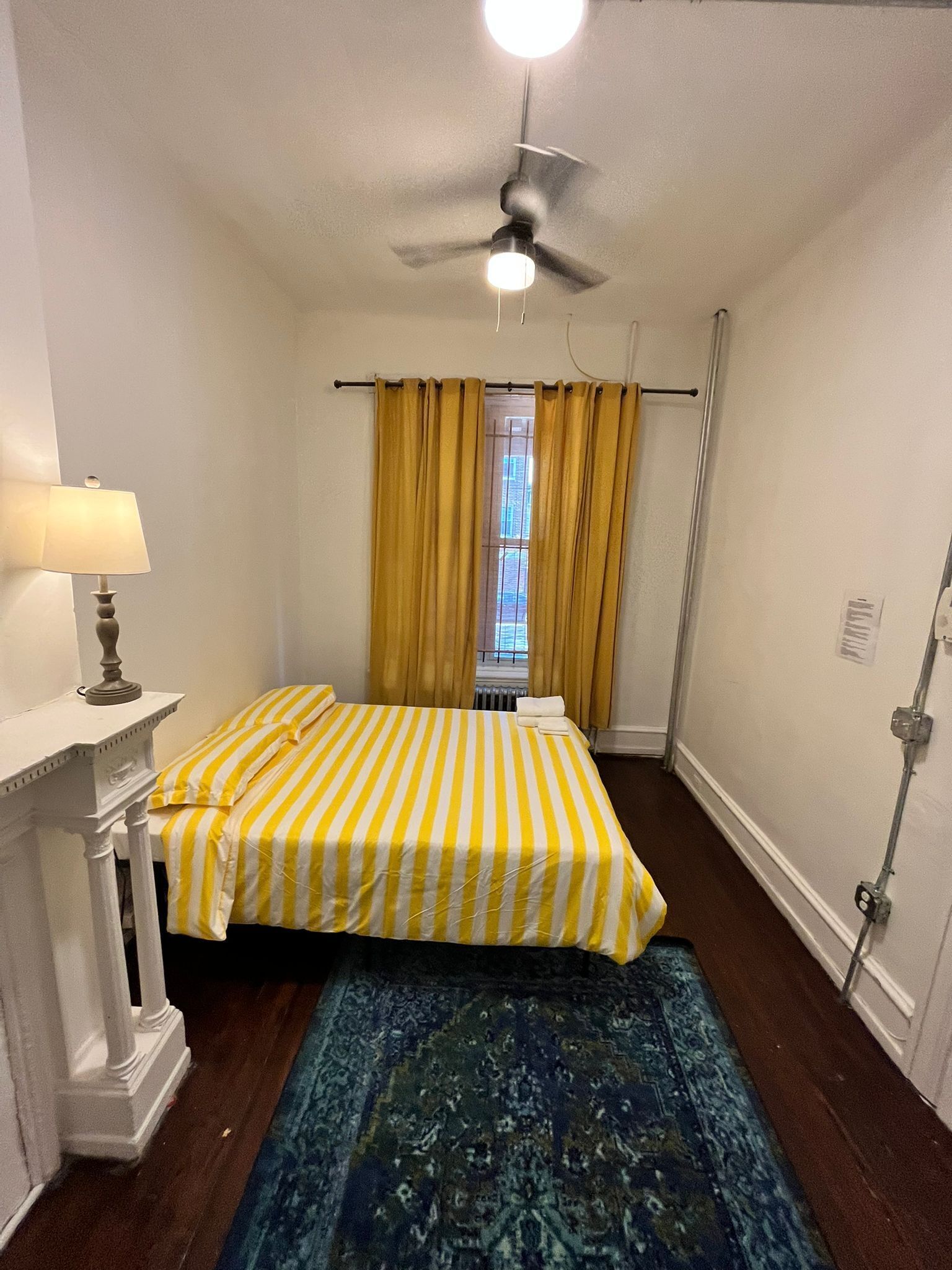 A room with a bed, a lamp, a ceiling fan, and a window with curtains.