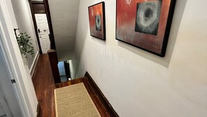 Ein Korridor mit Holzboden, einem beigefarbenen Teppich und zwei gerahmten abstrakten Gemälden an der Wand.
