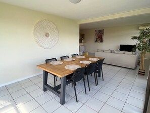 Un coin repas avec une table en bois et des chaises noires, une décoration murale blanche à texture, un canapé et une plante en pot.