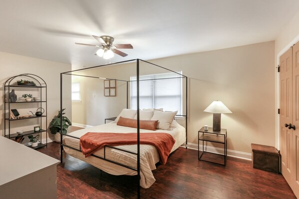 A four-poster canopy bed with a ceiling fan, a bedside table with a lamp, and a small shelf with decorative items. - Out of Town Workers Welcome - 10 minutes to LSU (Baton Rouge)