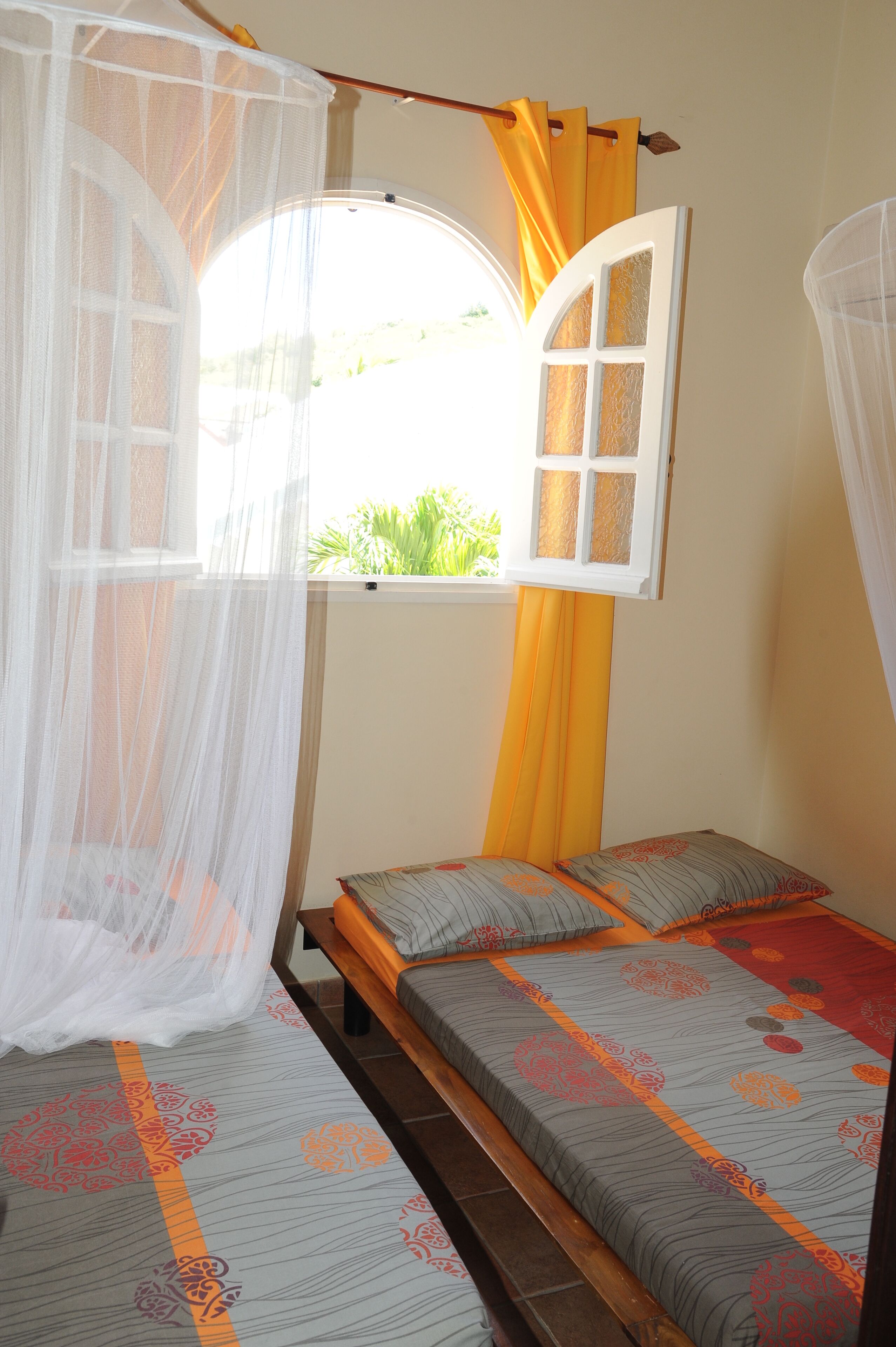 Une chambre à coucher avec un lit, une fenêtre avec des rideaux et une moustiquaire.