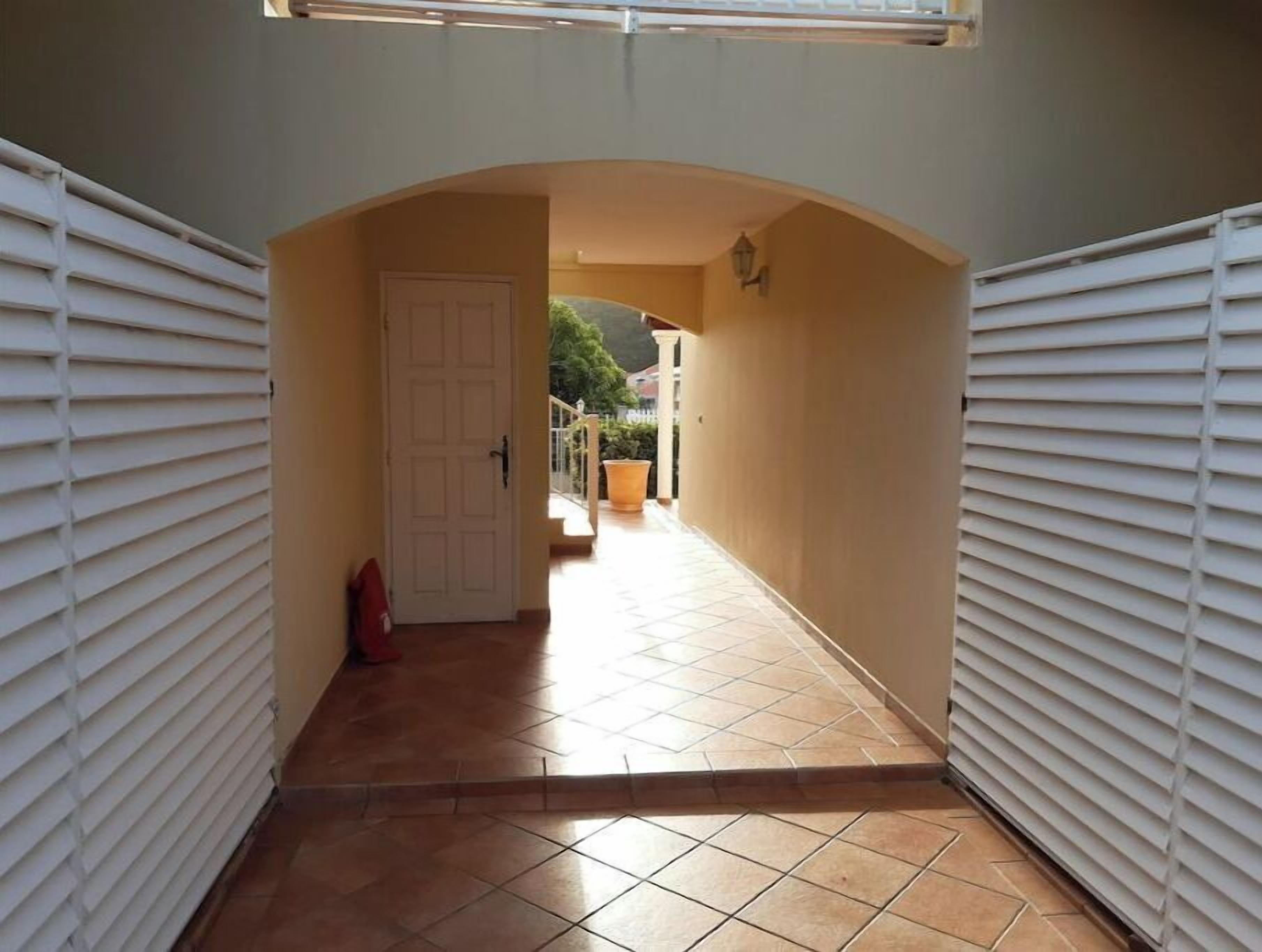 A narrow hallway with a tiled floor, white walls, and a door at the end.