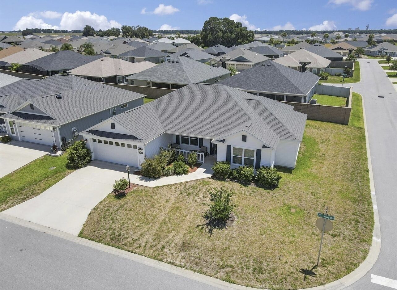 Un quartier résidentiel où les maisons se distinguent par leurs toits gris et leurs façades blanches, disposées selon un plan en damier, avec des pelouses bien entretenues et un ciel dégagé.