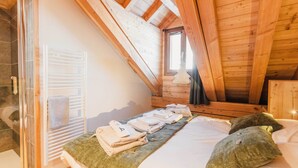 Une chambre mansardée chaleureuse avec un plafond en bois, un lit où les serviettes sont soigneusement pliées, et une fenêtre laissant entrer la lumière naturelle.