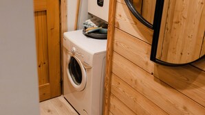 Une buanderie moderne et compacte, dotée d’un lave-linge à chargement frontal, de lambris en bois et d’un étendoir escamotable.