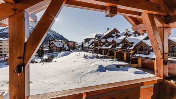 Un chalet en bois, dont le toit est recouvert de neige, et qui offre une vue sur une station de ski.