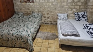 A room with two beds, a stone wall, and a wooden panel on one side. - Charming private studio near airport and (Persan)