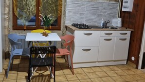 A compact kitchen with a dining area, featuring a small table, chairs, a stove, and a sink. - Charming private studio near airport and (Persan)