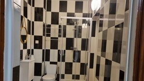 A bathroom with a checkered black and white tile wall, a toilet, a sink, and a glass-enclosed shower area. - Charming private studio near airport and (Persan)