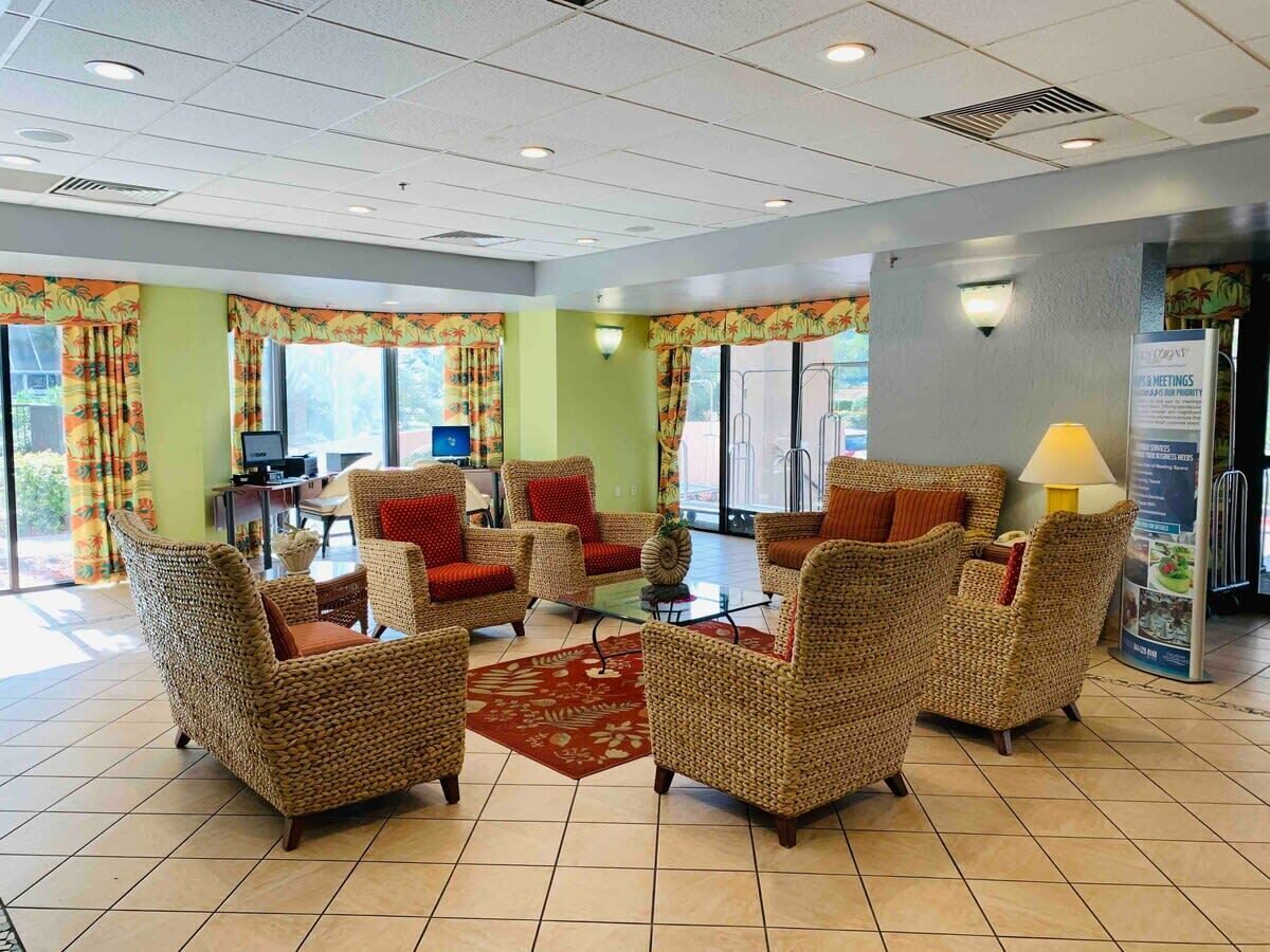A lobby with wicker furniture, a glass coffee table, and a red rug.