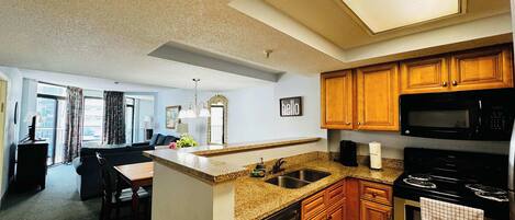 A modern kitchen with granite countertops, wooden cabinets, a stainless steel dishwasher, and a black microwave.