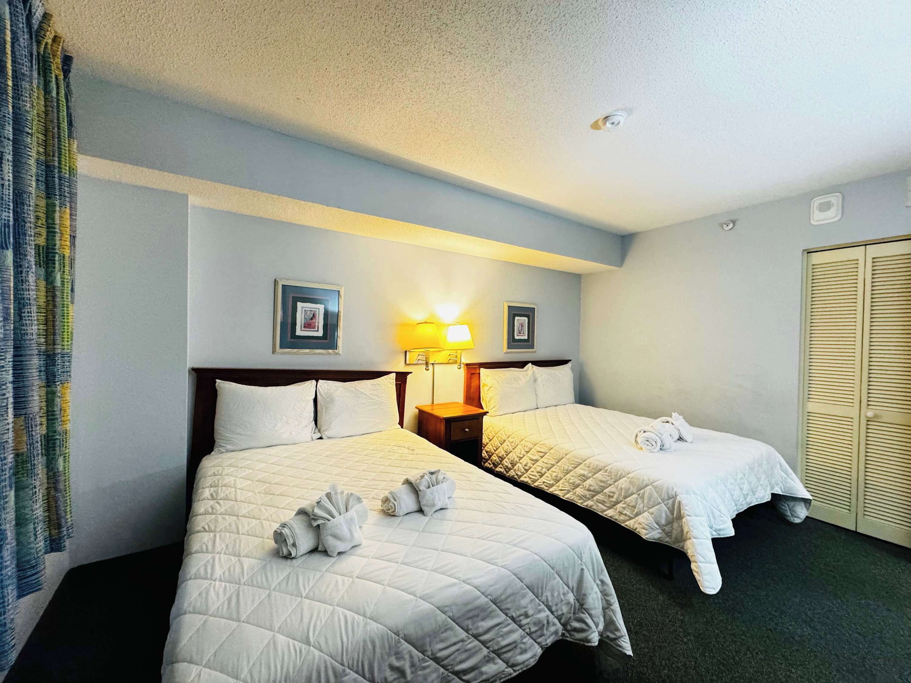 A hotel room with two beds, a nightstand, a lamp, and a wardrobe.