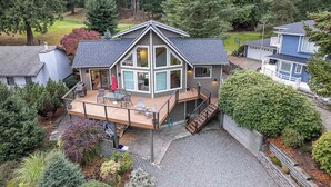 A modern house with a large deck, a covered patio, and a view of the surrounding forest.