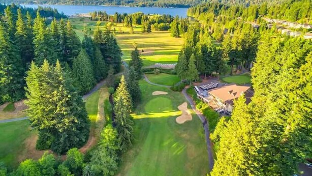 A golf course with a clubhouse, surrounded by dense forest and mountains.