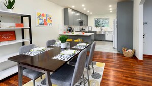 A modern kitchen with grey cabinets, a dining area with a wooden table, and a view of the adjacent living space.