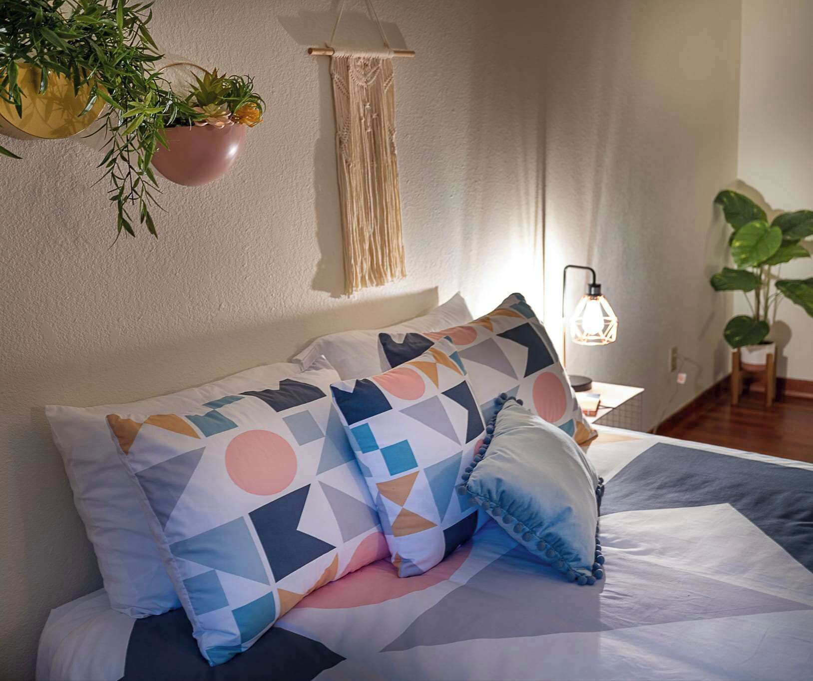Un lit agrémenté d’oreillers aux motifs géométriques, une décoration murale en macramé et des plantes en pot.