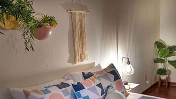 Un lit agrémenté d’oreillers aux motifs géométriques, une décoration murale en macramé et des plantes en pot.