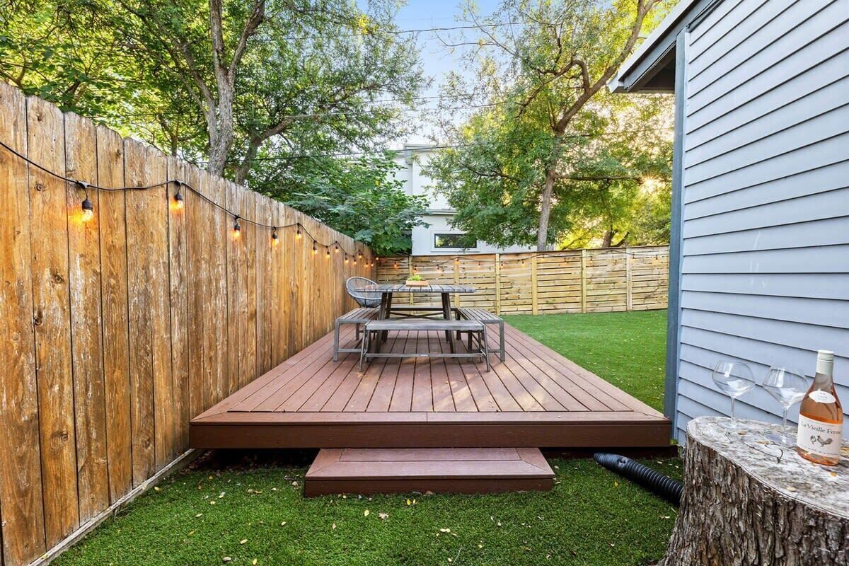 A wooden deck with a table and chairs, surrounded by a wooden fence and a house.