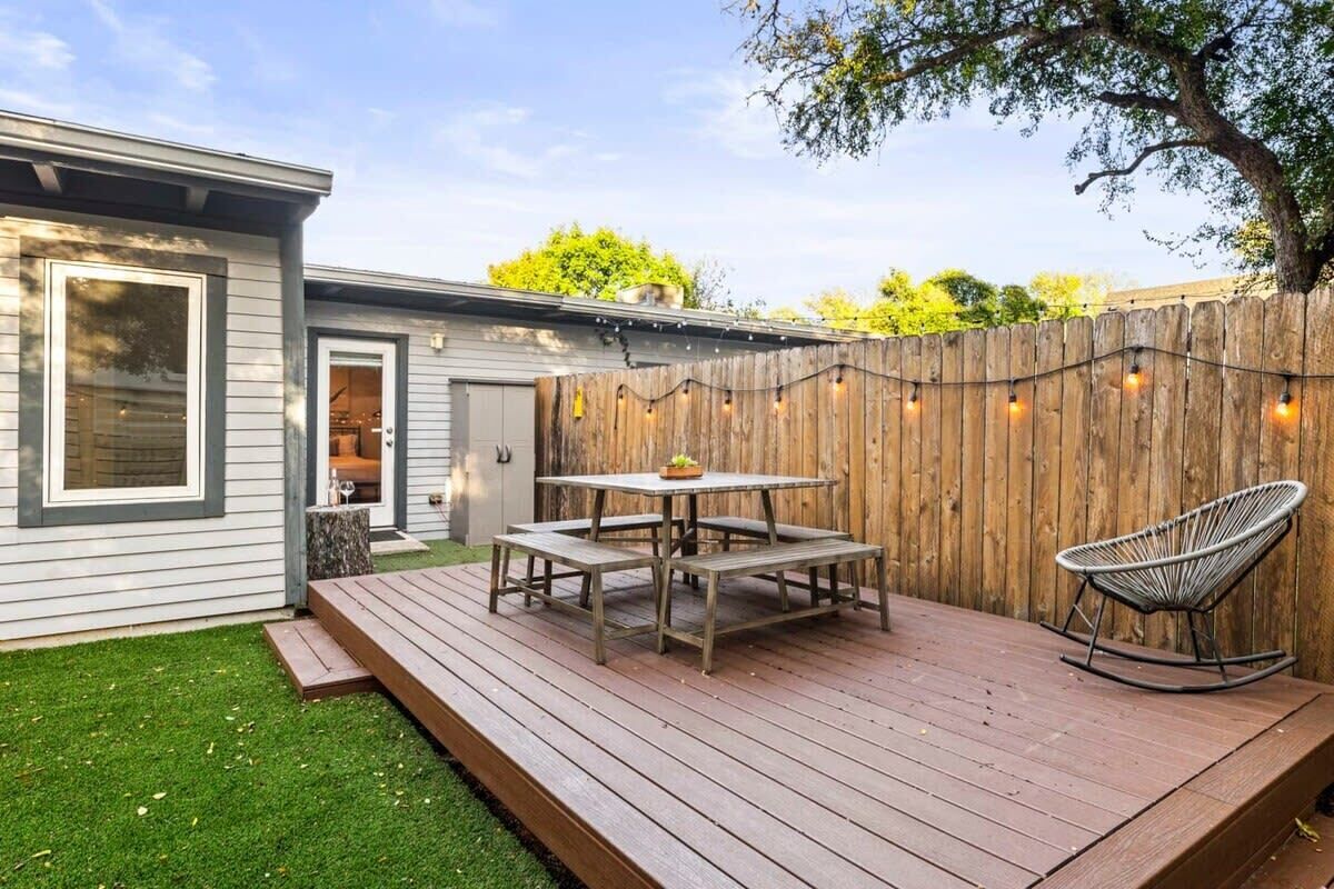 A wooden deck with a table and chairs, a rocking chair, and a string of lights.