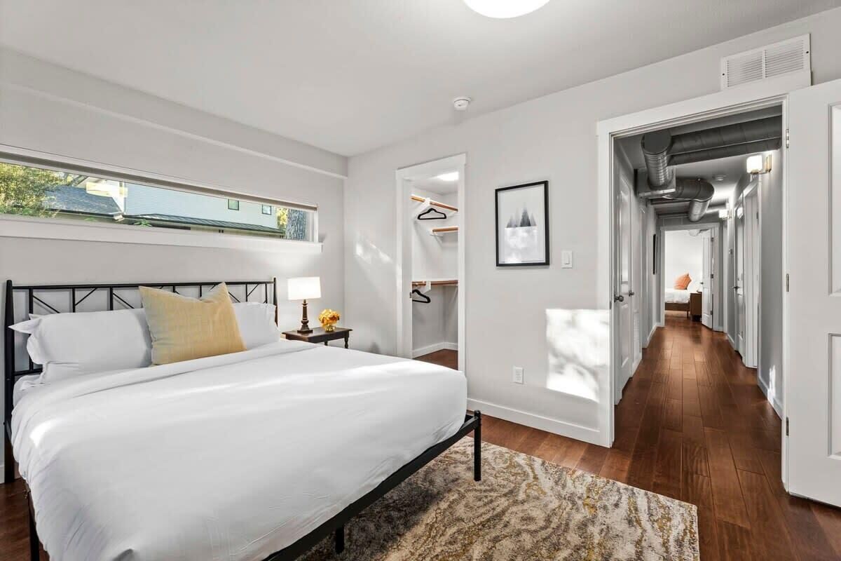 A bedroom with a bed, bedside table, lamp, and a view of the outside.