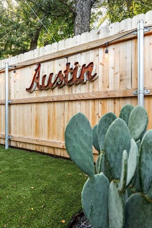 A wooden fence with the word 'Austin' mounted on it, a cactus in the foreground, and a metal pole to the left.