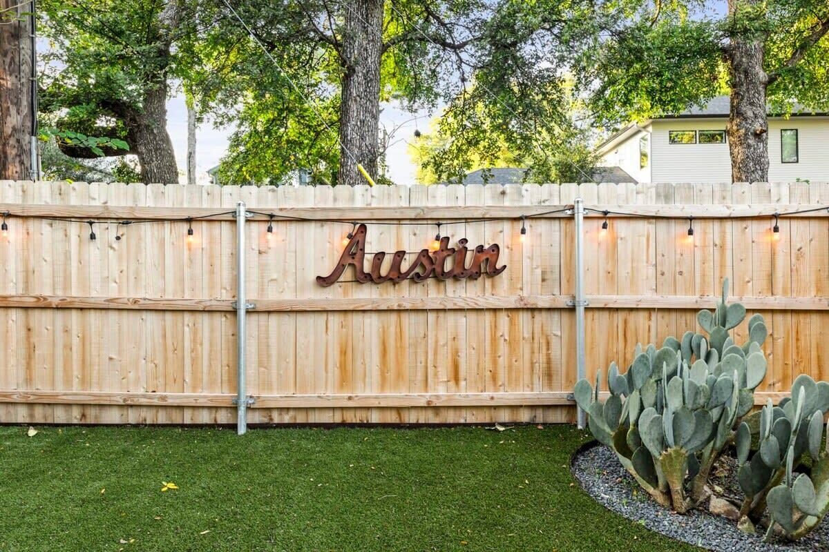 A wooden fence with the name 'Austin' in metal letters, a cactus plant, and a grassy area.