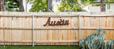 A wooden fence with the name 'Austin' in metal letters, a cactus plant, and a grassy area.