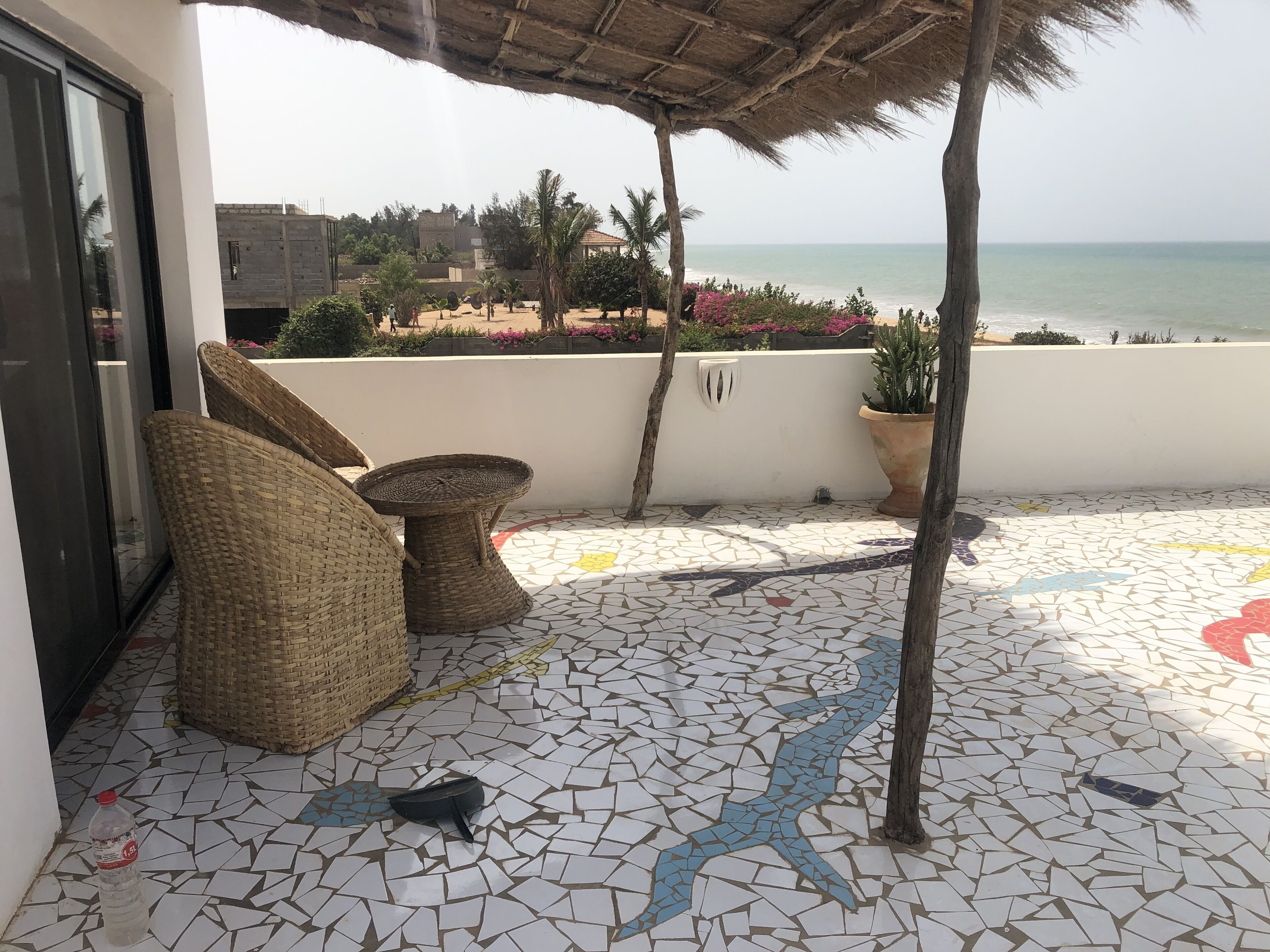A tiled patio with wicker furniture, a potted plant, and a view of the beach and ocean.