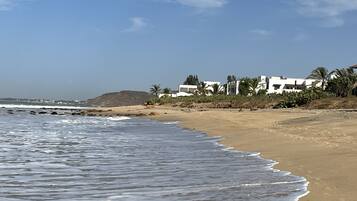 A beach with waves, a sandy shore, and white buildings with palm trees.