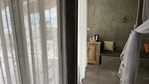 A room with a stone wall, a wooden cabinet, a bed with a white canopy, and a view through sheer curtains. - Bine Bassile (Guereo)