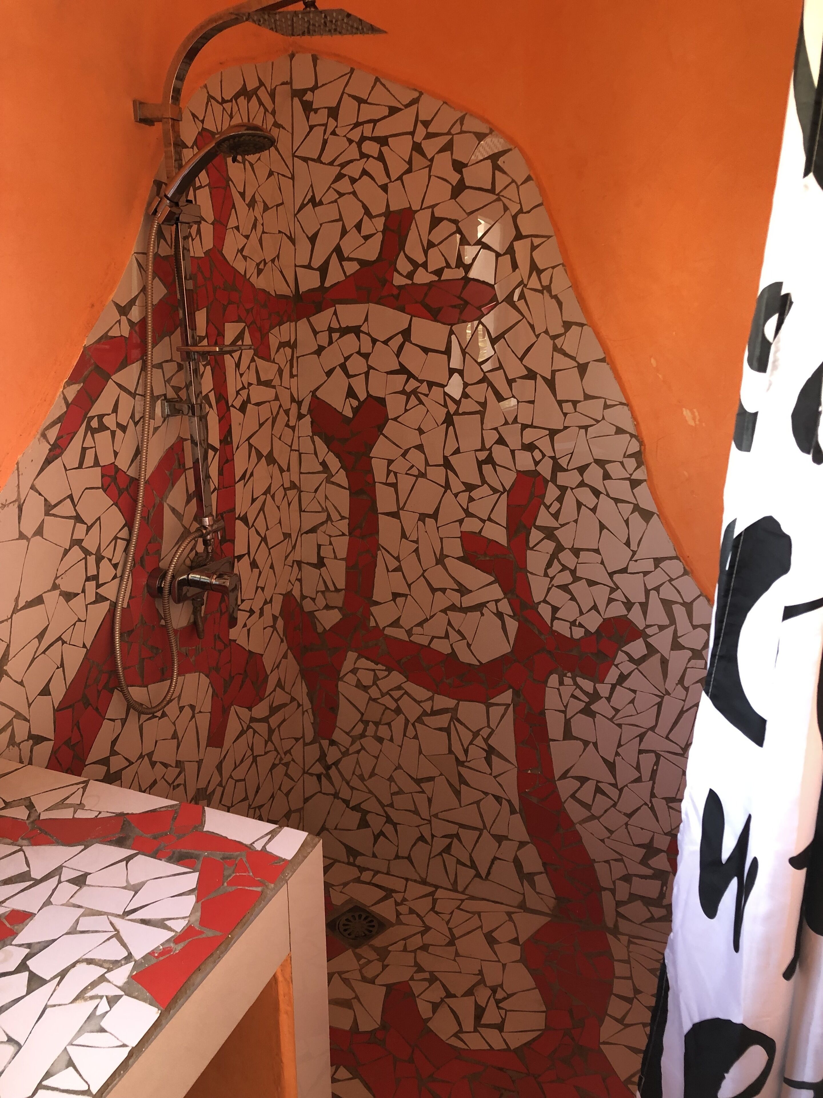 A bathroom with a mosaic wall, a shower, and a sink.