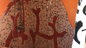 Un baño con pared de mosaicos, ducha y lavamanos.