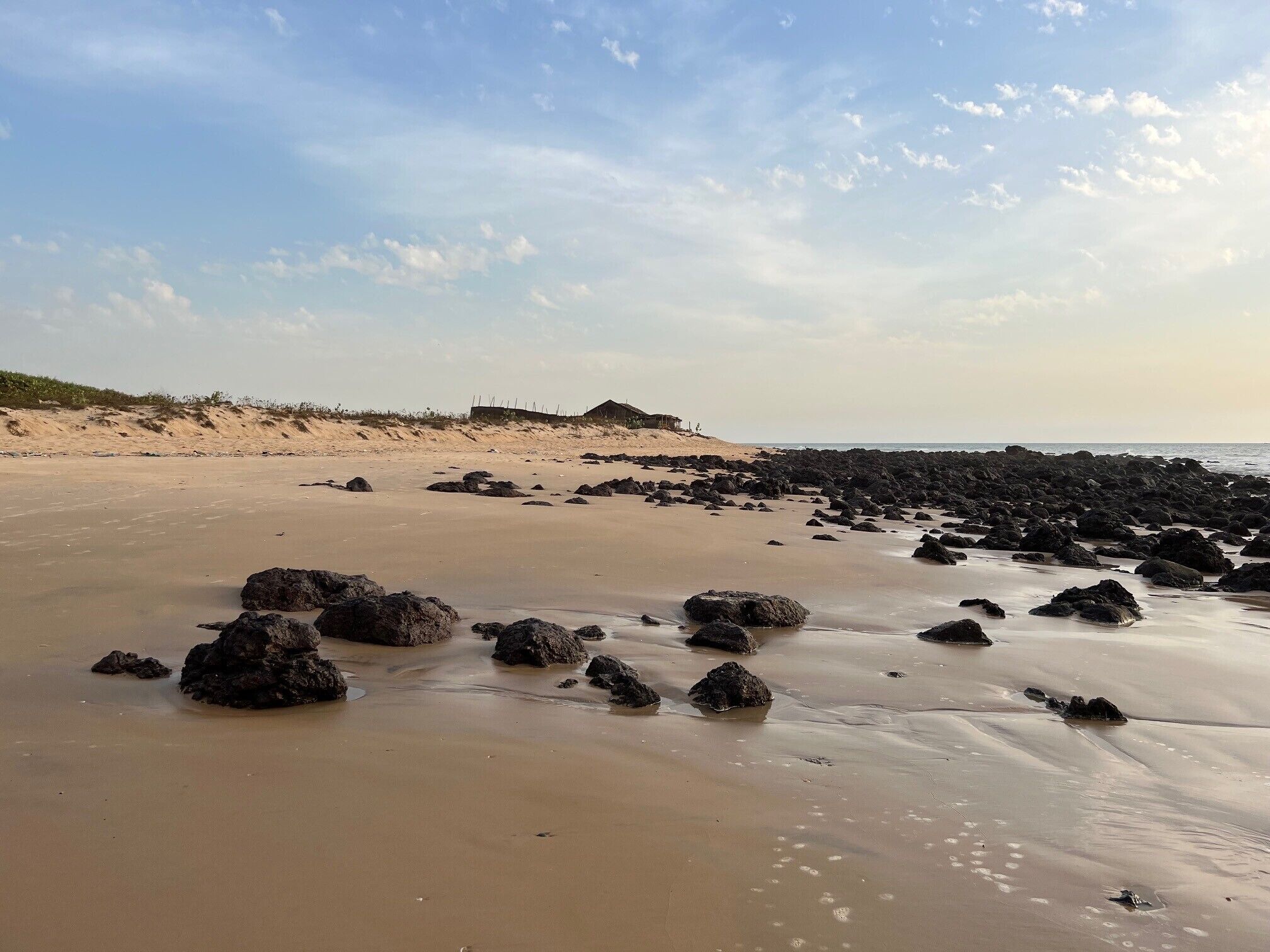 Una playa con rocas dispersas y una duna al fondo.