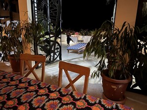 Un coin repas avec une table dressée pour deux personnes, entouré de plantes en pot et agrémenté d’une grille décorative en métal.