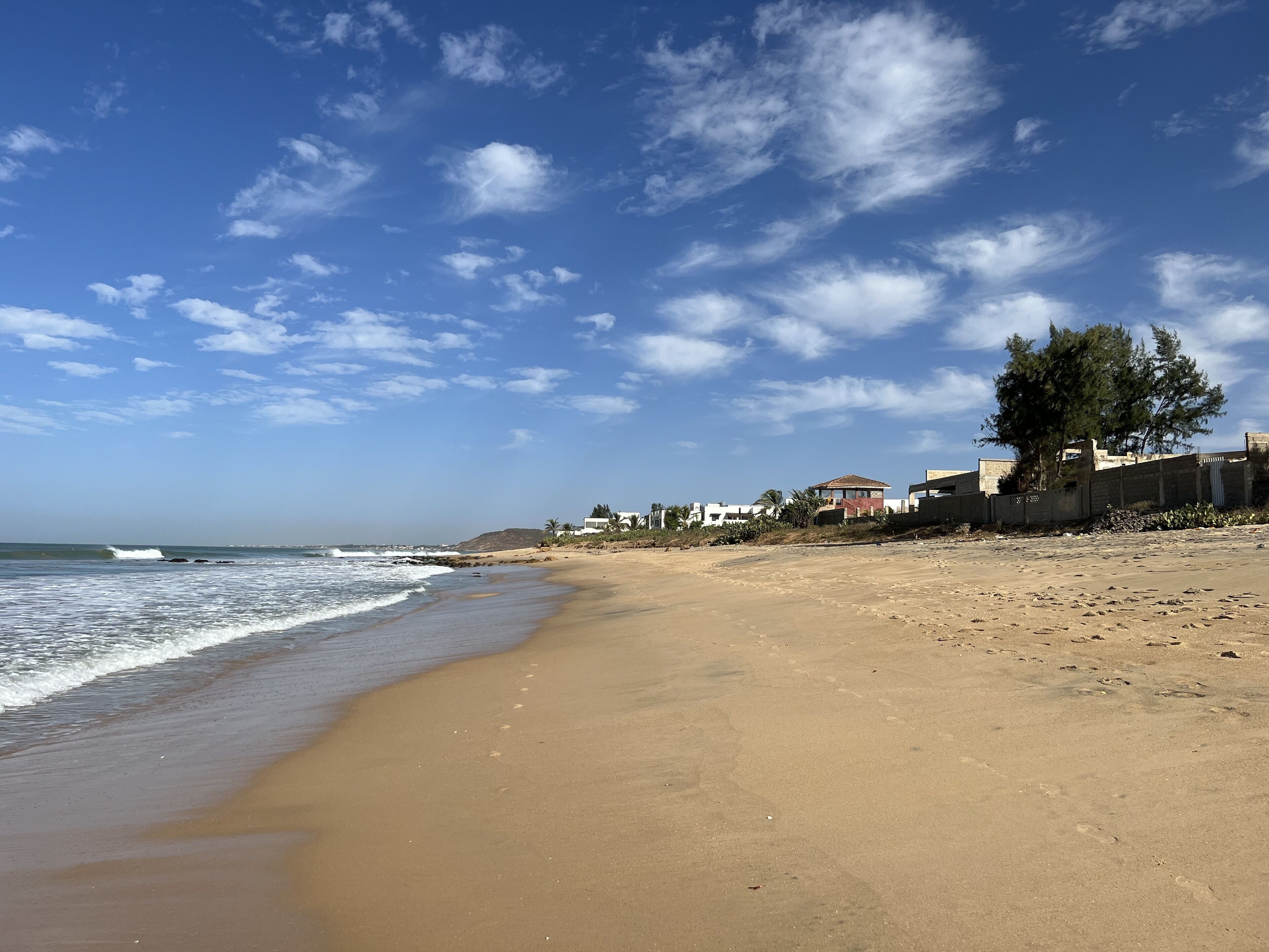 Une plage de sable avec des vagues, un ciel dégagé et des bâtiments en arrière-plan.