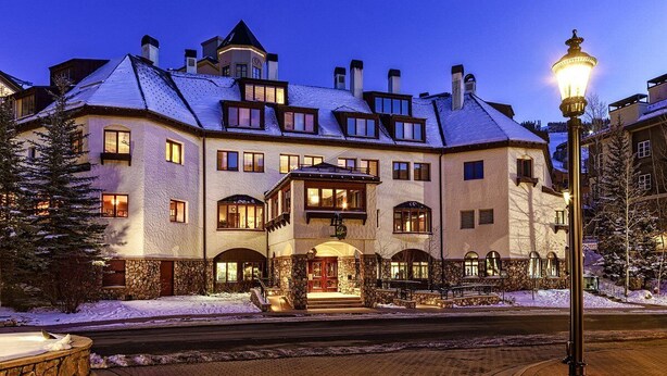 Un edificio grande de varios pisos con techo cubierto de nieve y base de piedra. Cuenta con varias ventanas, una entrada central con arco de piedra y un pequeño balcón.