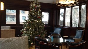 Una habitación acogedora con un árbol de Navidad, sillones de cuero, una mesa redonda y grandes ventanales con vistas a edificios.