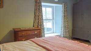 Une chambre à coucher comprenant un lit, une commode, une armoire et une fenêtre avec des rideaux.