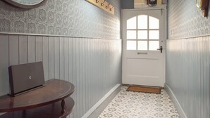 Un couloir avec une porte blanche, un papier peint à motifs, une table ronde avec un ordinateur portable et un porte-manteau suspendu.