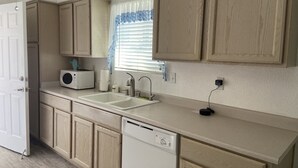 Une cuisine avec des meubles de rangement en bois, un plan de travail blanc, un évier, un four à micro-ondes et un lave-vaisselle.