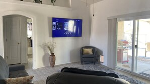 Un salon avec un téléviseur à écran plat fixé au mur, un fauteuil gris, un canapé et un vase décoratif posé sur le sol.