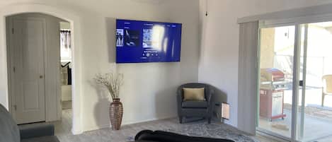 En stue med et fladskærms-tv monteret på væggen, en grå lænestol, en sofa og en dekorativ vase på gulvet.