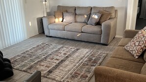 Un salon avec un canapé beige, un tapis à motifs et un élément décoratif mural.