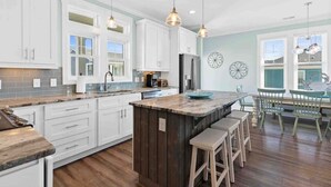A kitchen with white cabinets, a central island with stools, pendant lighting, and a view of the outside.