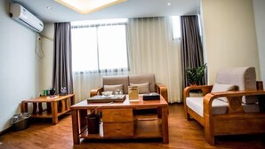Une chambre d’hôtel moderne avec un plancher en bois, un canapé, une table basse en bois, une petite table avec une lampe et une grande fenêtre avec des rideaux.