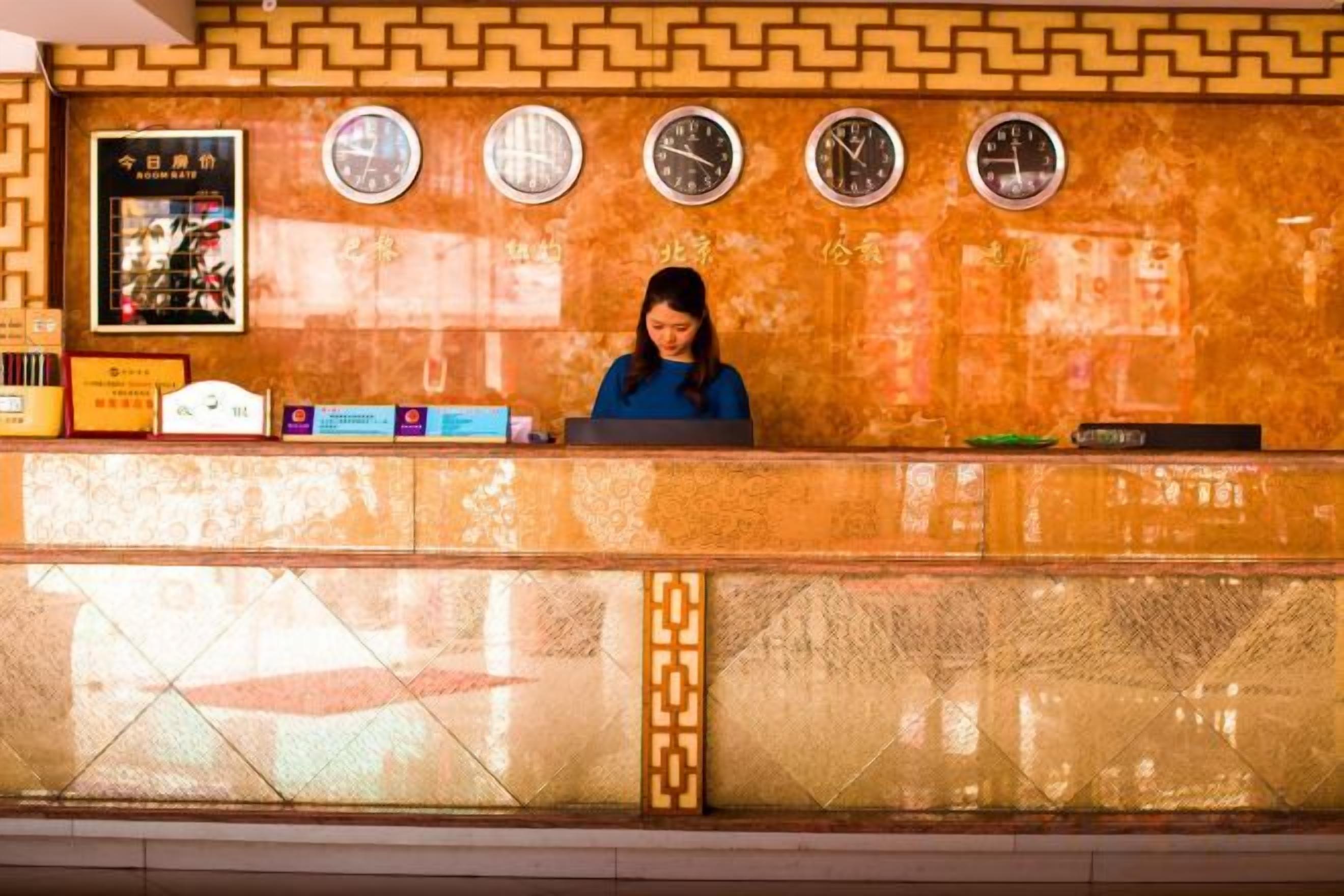 A hotel reception desk with clocks, a poster, and a counter with various items.