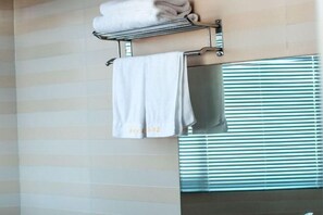 Une salle de bain équipée d’un porte-serviettes où sont posées deux serviettes, d’un miroir et d’une fenêtre avec des stores.
