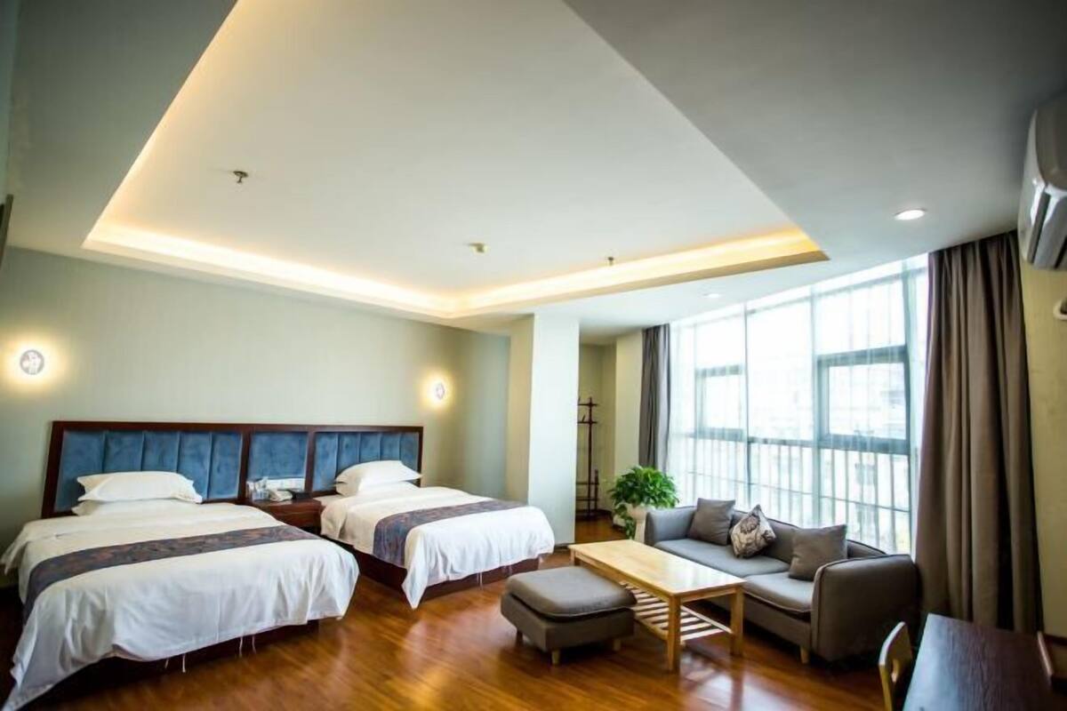 Une chambre d’hôtel avec deux lits, un canapé, une table basse et une grande fenêtre.